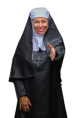 Middle age senior christian catholic nun woman over isolated background smiling friendly offering handshake as greeting and welcoming. Successful business.