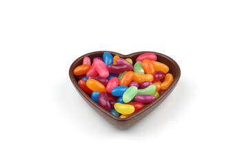 multi-colored sweet candies in heart shaped bowl on white background, top view. Space for text