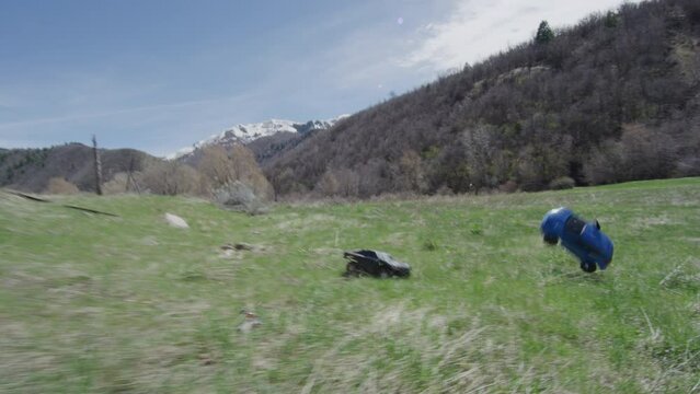 Two RC cars driving off road and tumbling through grass field