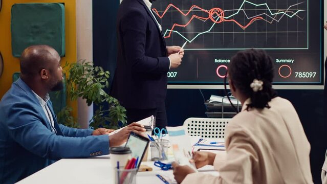 Project team colleagues examining sales infographics on presentation, reviewing annual reports to understand what needs to change in order to expand the business internationally. Camera A.