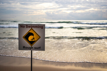 No swiming warning sign on the beach at sunset
