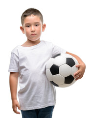 Dark haired little child playing with soccer ball with a confident expression on smart face thinking serious