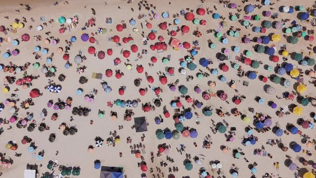 Aerial top down view of people and colorful sun umbrellas enjoying the sun on sunny beach in Rio de Janeiro