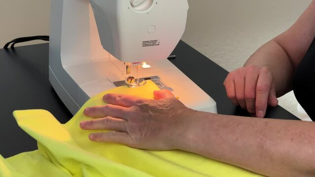 4K HD video of older caucasian female hands working with sewing machine, sewing border edge on flannel blanket. Coming to a corner, turning and resuming sewing, removing pins as she works.