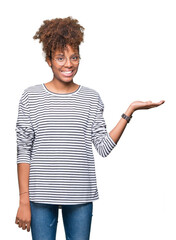 Beautiful young african american woman wearing glasses over isolated background smiling cheerful presenting and pointing with palm of hand looking at the camera.