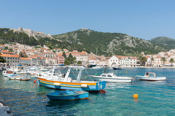 Castle on hill above Hvar township with picturesque small boats moored in harbour - obrazy, fototapety, plakaty