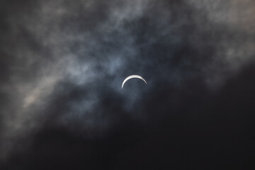 Partial solar eclipse - moon covers sun, dark clouds, celestial drama - crescent sun - atmospheric...