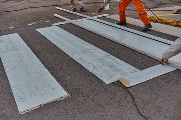 Three men in orange work clothes are painting a crosswalk