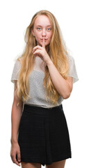 Blonde teenager woman wearing moles shirt asking to be quiet with finger on lips. Silence and secret concept.