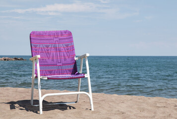 colorful folding beach chair on a sandy beach near the ocean with a blue sky