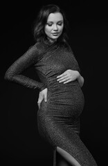 Black and white portrait of pregnant female in sequin dress with hands near pregnant belly.