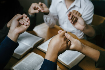 Obraz na płótnie Canvas Christian Family prayer and worship. Christian group of people holding hands and praying worships to believe and Bible on a wooden table prayer meeting concept. Church Community pray together