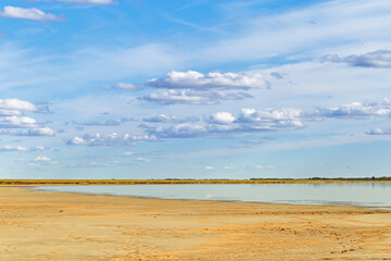 Beautiful shore of lake, white clouds on sky, water surface and sandy beach. Tranquil nature scene,...