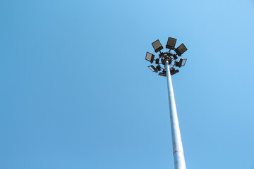 Spotlight hanging on high metal pole with blank blue sky background