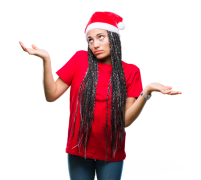Young braided hair african american girl wearing christmas hat over isolated background clueless and confused expression with arms and hands raised. Doubt concept.
