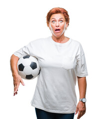 Atrractive senior caucasian redhead woman holding soccer ball over isolated background scared in...
