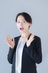 Woman in business suit in surprised pose with open hand looking at camera