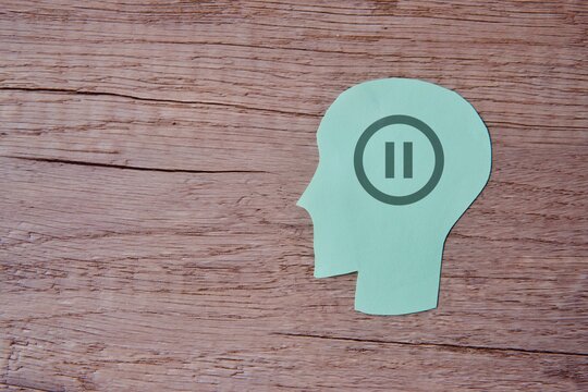 A green paper cut-out of a human head with a pause button icon. Copy space for text. Rest, take a break concept.