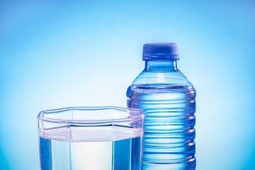 A glass with water and plastic bottle on a blue background.