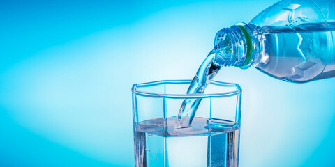 Pouring water from a bottle into a glass on a blue background. Banner with place for text.