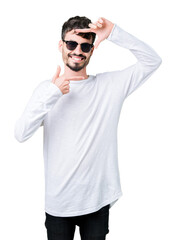 Young handsome man wearing sunglasses over isolated background smiling making frame with hands and fingers with happy face. Creativity and photography concept.