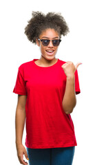 Fototapeta na wymiar Young afro american woman wearing sunglasses over isolated background smiling with happy face looking and pointing to the side with thumb up.