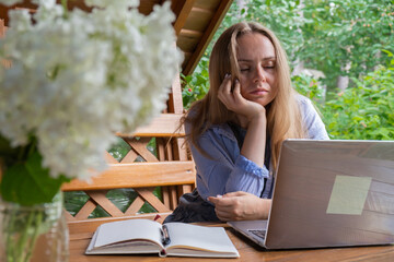 Upset sleepy Female student has online lesson education outdoor in garden wooden alcove. Blonde woman sitting outside work on laptop having video call