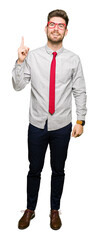 Young handsome business man wearing glasses pointing finger up with successful idea. Exited and happy. Number one.