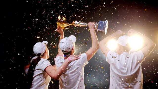Team of four young winners together celebrates success and jump for joy, raising arms and victory trophy up. Happy award, triumph achievement in sport competition