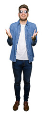 Young handsome elegant man wearing denim jacket celebrating mad and crazy for success with arms...