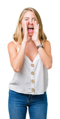 Beautiful young woman over isolated background Shouting angry out loud with hands over mouth