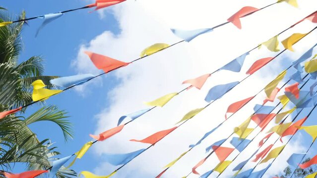 Colorful triangle bunting flags or banderitas hanging and blown by wind against blue sky. Celebration and fiesta concept.