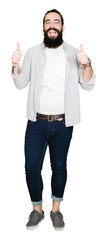 Young man with long hair, beard and earrings success sign doing positive gesture with hand, thumbs up smiling and happy. Looking at the camera with cheerful expression, winner gesture.