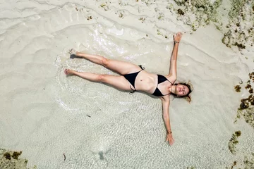 Foto op Canvas Top aerial drone view of woman in swimsuit relaxing and sunbathing on beach Near The Ocean. Attractive brunette girl in black bikini laying on sandy coast. © diy13