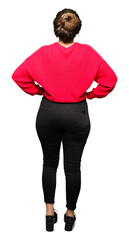Young beautiful woman wearing red sweater and bun standing backwards looking away with arms on body