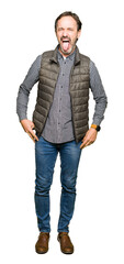 Middle age handsome man wearing winter vest sticking tongue out happy with funny expression. Emotion concept.