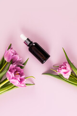 Cosmetic product, serum, oil for face and body skin care in a dark glass bottle with a dropper. Top vertical view. Spring flowers.