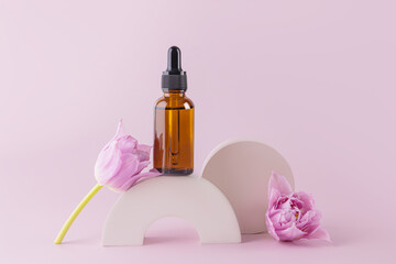 Fashion beauty product, serum in glass cosmetic bottle with dropper for face and body skin care standing on a round cement podium with a tulip flower