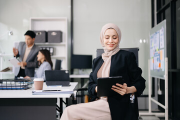 Young Arabic female entrepreneur wearing a hijab working online with a laptop at modern office.