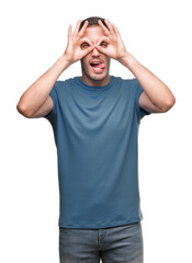 Naklejka premium Handsome young casual man doing ok gesture like binoculars sticking tongue out, eyes looking through fingers. Crazy expression.