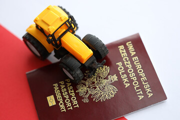 Red polish passport and yellow tractor on smooth red and white flag of Poland close up