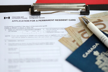 Application for permanent resident card on table with pen and canadian passport with money close up