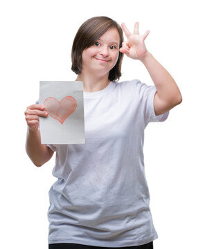Young adult woman with down syndrome holding red heart card over isolated background doing ok sign with fingers, excellent symbol