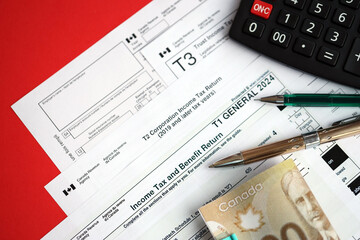 Many blank Canadian tax forms lies on table with canadian money bills, calculator and pen close up. Taxation and annual accountant paperwork in Canada