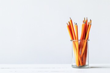 A Glass Jar Full of Orange Pencils on a White Wooden Table Against a Plain Background