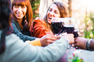 Close friends sharing a joyful toast with red wine outdoors - women celebrating togetherness with...
