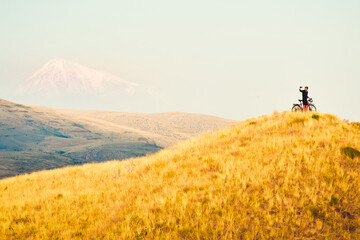 joyful caucasian male cyclist standing by touring bicycle looking to camera on top hilltop happy...