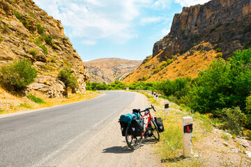 Loaded with bags red bicycle stands on the side of the road surrounded by countryside in armenia,...