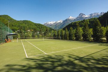 A tennis court with green grass on a sunny summer day in nature with a view of the snow-capped...