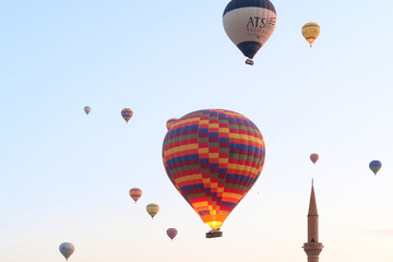 Hot air balloons in the early morning over the town of Göreme with the tower of a Minaret right next to it, Göreme, Cappadocia, Turkey